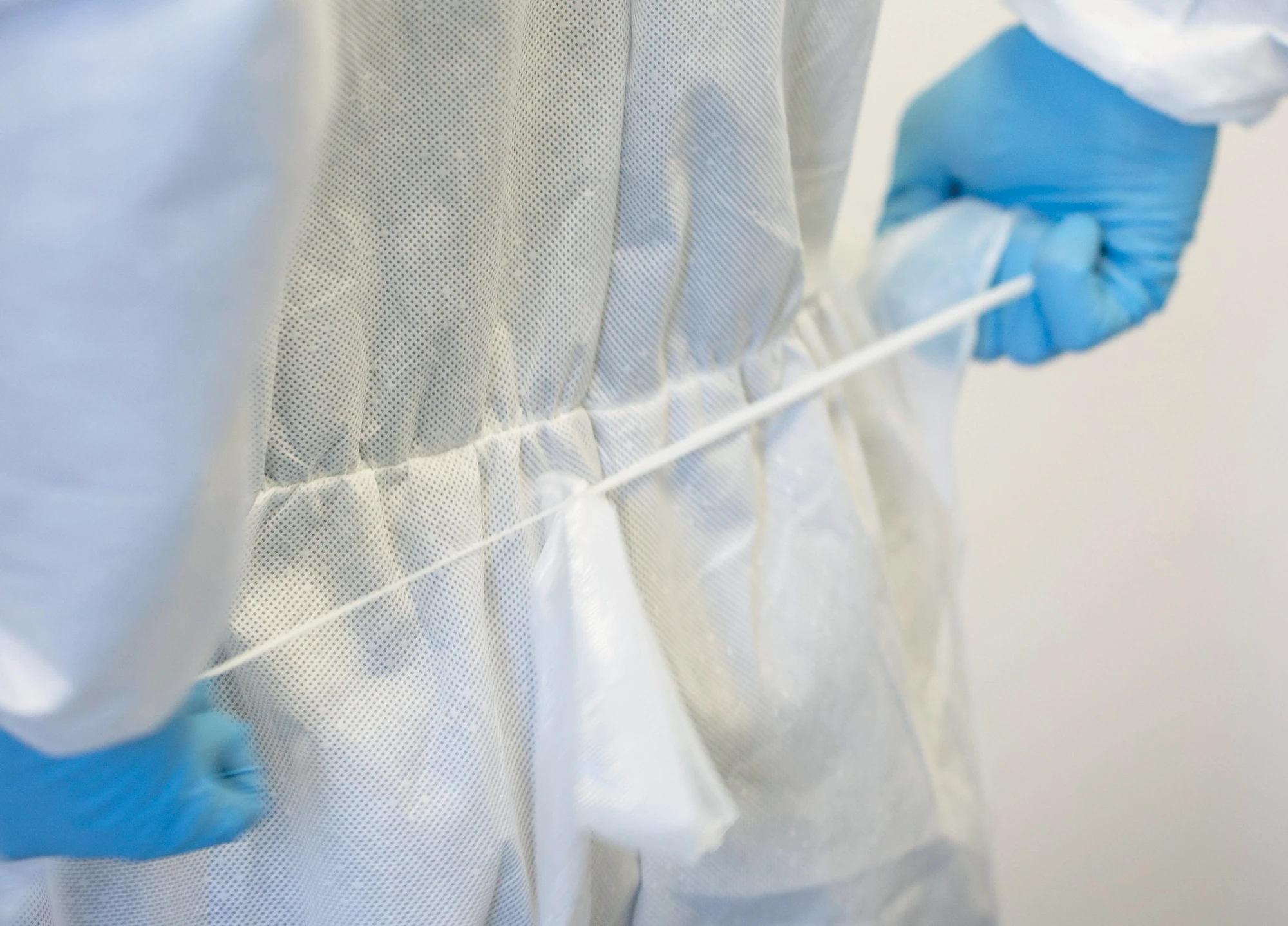 Close-up van onderzoeker in beschermend laboratoriumpak met blauwe handschoenen.